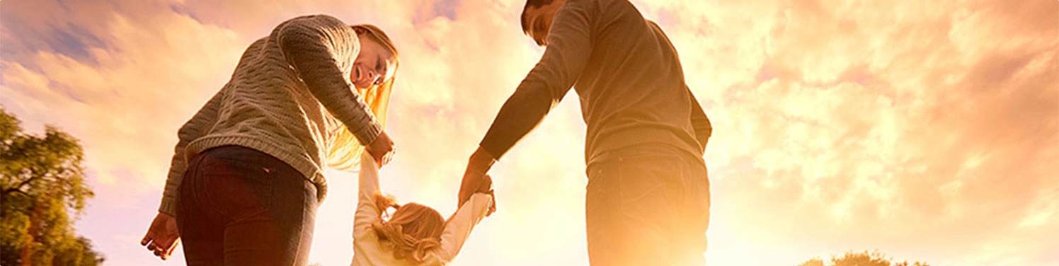 two parents each holding the hand of their child with a sunset scene in the background